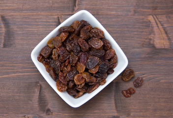 Raisins in square bowl on wooden table top view