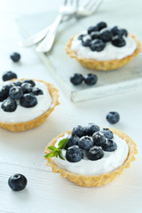 Dessert tartlets with blueberries on white wooden background