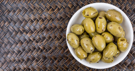 Pickled olive in a white bowl over wicker background