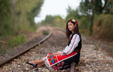 Girl with bulgarian costume sitting on the railway line