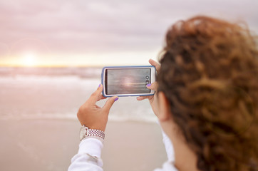 Curly girl photographing  the sunrise at the ocean