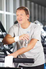 Fototapeta na wymiar Älterer Mann trinkt Wasser im Fitnesscenter