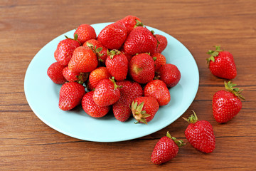 Ripe strawberries in plate on wooden table, closeup