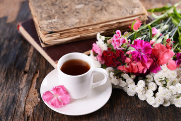 Fototapeta na wymiar Old books with beautiful flowers and cup of tea on wooden table close up