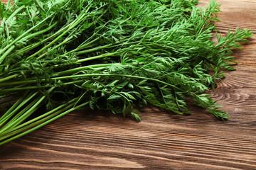 Green tops of organic carrots on wooden table, closeup
