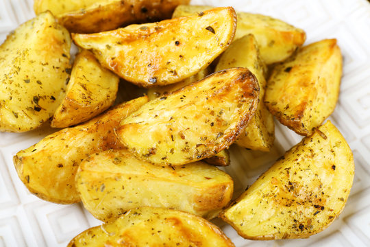 Baked spicy potatoes on white plate, closeup