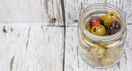 Pickled olive in a mason jar over wooden background