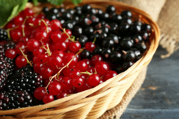 Ripe red and black currant in wicker basket on wooden background