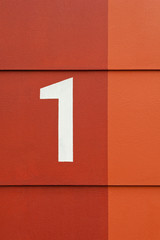 Hausnummer 1 in weiss auf einer Wand in rot und orange
