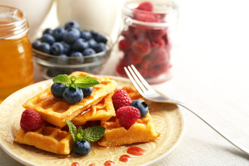 Sweet homemade waffles with forest berries and sauce on table background