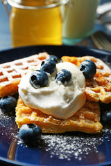 Sweet homemade waffles with blueberries and cream on plate, on dark wooden background