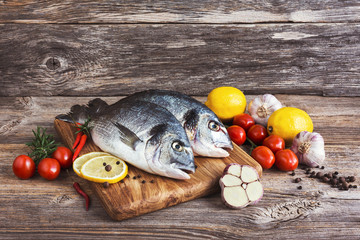 Fresh dorada fish on wooden cutting board with vegetables