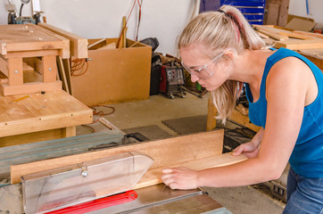 Young adult female woodworker cutting board on table saw.
