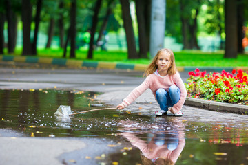 Little happy girl having fun in a large puddle in autumn park