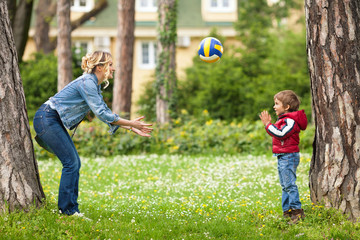 Cute little boy throwing a ball to his mother during the play in a park