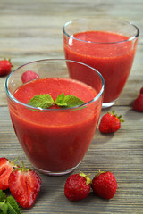 Glasses of strawberry smoothie with berries on wooden table close up