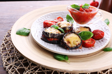 Dish of eggplant with cherry tomatoes and cheese in white plate on wooden table, closeup