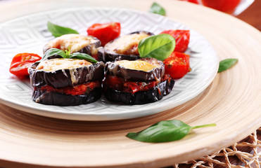 Dish of eggplant with cherry tomatoes and cheese in white plate on wooden table, closeup