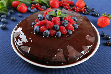 Delicious chocolate cake with summer berries on blue tablecloth, closeup