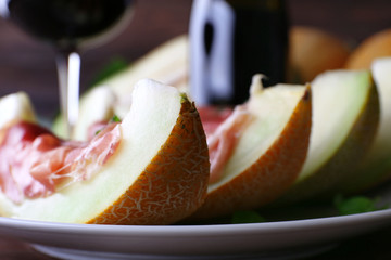 Melon with prosciutto of Parma ham on wooden table, closeup