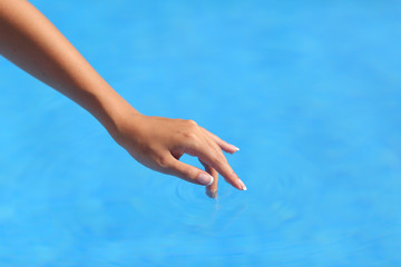 Beautiful woman hand touching blue water in a pool