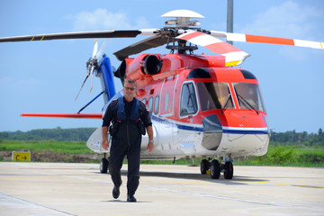 caucasian offshore helicopter pilot is walking and smiling besid