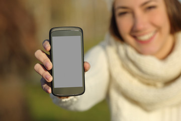 Woman showing a smart phone screen in winter outdoors