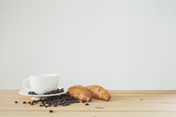 coffee cup and croissant on wooden table over white background.