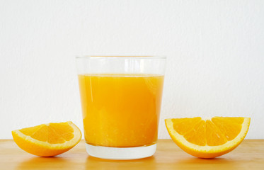 Glass of orange juice with sliced orange on wooden table