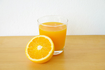 Glass of orange juice with sliced orange on wooden table