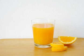 Glass of orange juice with sliced orange on wooden table