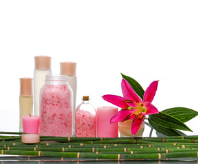 Spa setting with pink lily and bamboo grove and massage oil , salt in glass ,candle 

