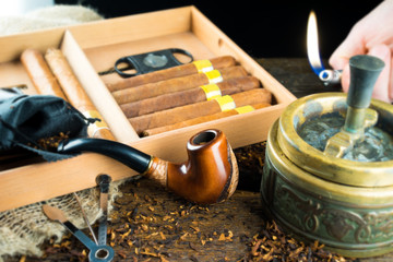 Pipe lies next to a box of cigars and an ashtray