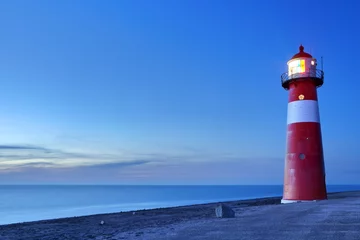 Fototapete Leuchtturm Rot-weißer Leuchtturm und ein klarer Himmel in der Abenddämmerung