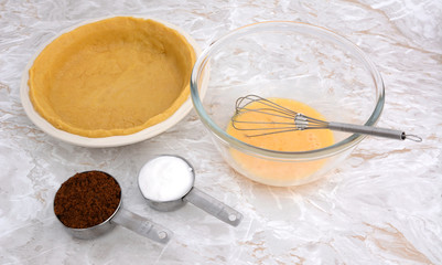 Lined pie dish, beaten egg and measuring cups of sugar