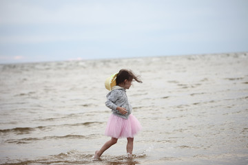 Little girl walking in waves against sea and sky