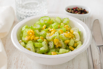 salad celery with corn in white bowl on white wooden background