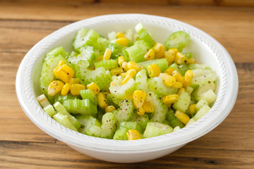 salad celery with corn in white bowl on brown background