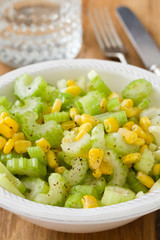 salad celery with corn in white bowl on brown wooden background