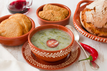 portuguese soup caldo verde in ceramic dish and spoon with corn bread and appetizers