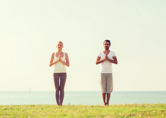 smiling couple making yoga exercises outdoors