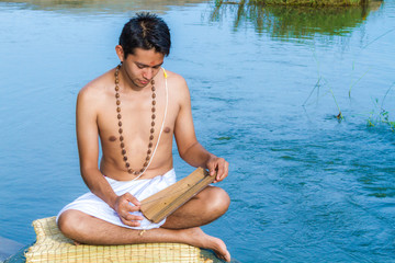 A young brahmin reads and ancient Hindu scripture on a river bank in India 
