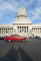 Fototapeta na wymiar Shadows of pedestrians passing in front of classic American car near the Capitolio building in Central Havana