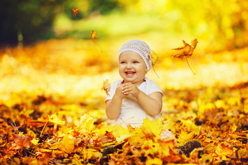 Portrait of happy little baby playing with yellow autumn leaves