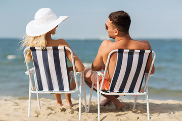 happy couple sunbathing in chairs on summer beach