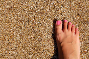 Wet female feet by water on sand