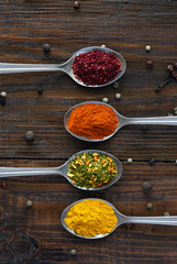Variety of Eastern Spices in Silver Spoons Close up Image of Grey Metal Spoons with Selection of Aromatic Seasonings on Rough Dark Natural Wooden Board Table Vertical