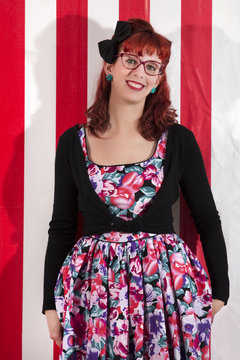View of pinup young woman in vintage style clothing next to red and white striped tents.