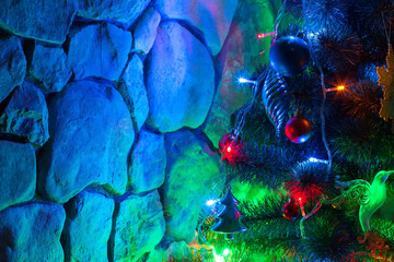 Fototapeta na wymiar Christmas tree decorated with colored lights and toys on the background of a stone wall at night