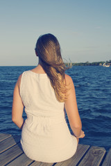 Woman sitting on dock, looking toward ocean